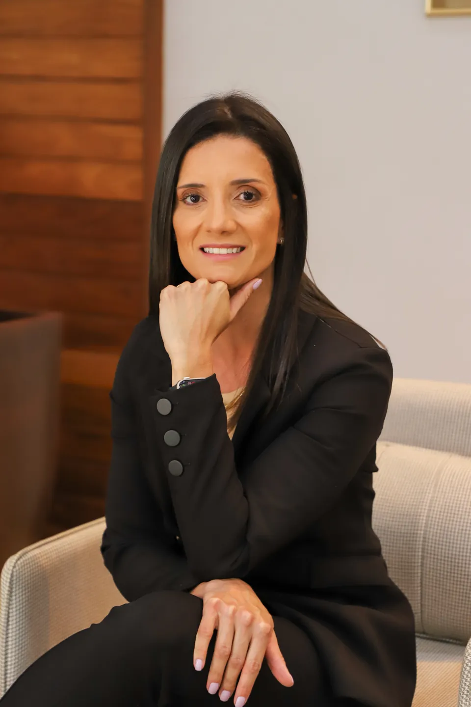 Dra. Anaísa Ramos de blazer preto, sentada numa poltrona no consultório